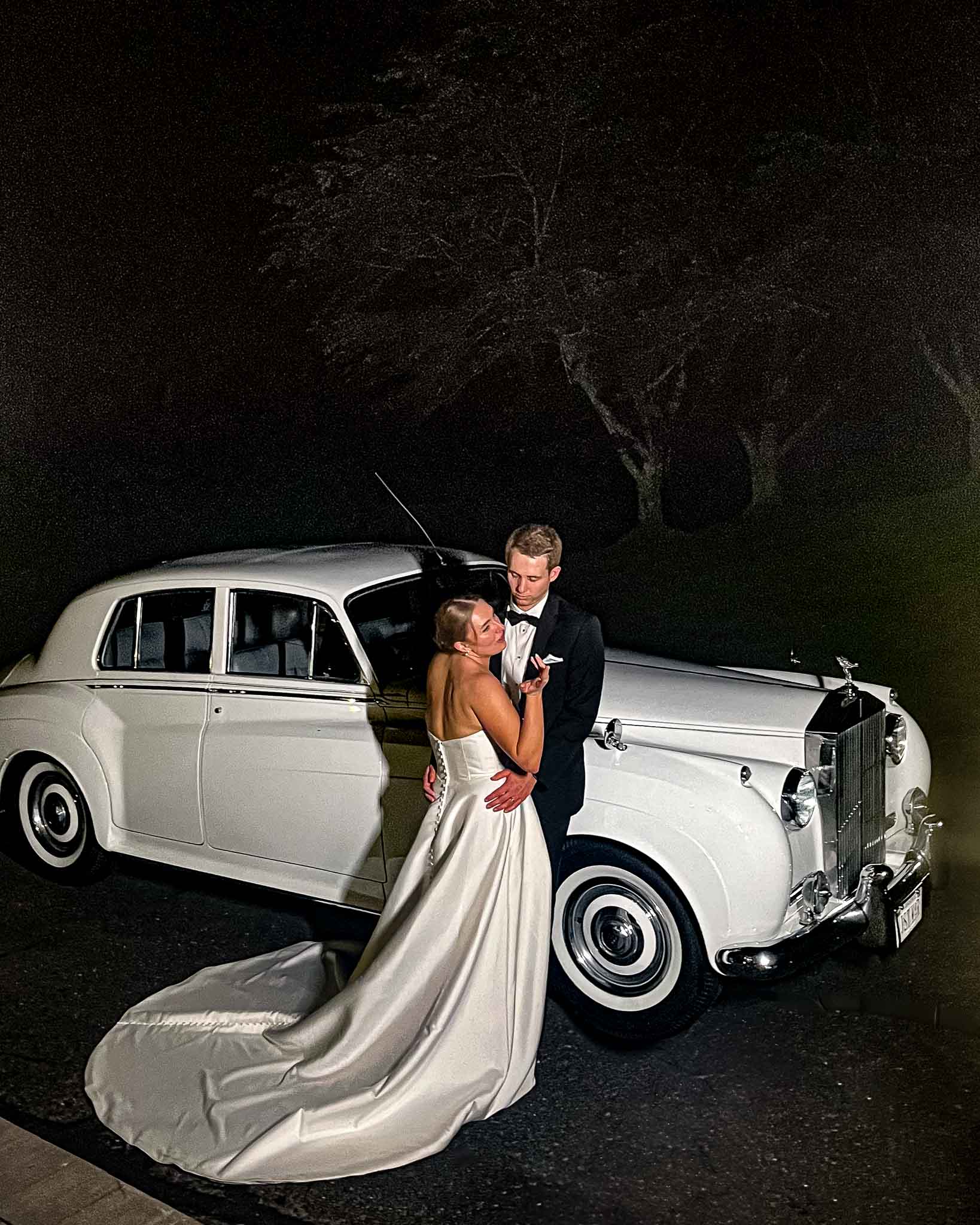 Photo of bride-groom standing next to our white 1956 Rolls Royce during an evening celebration.